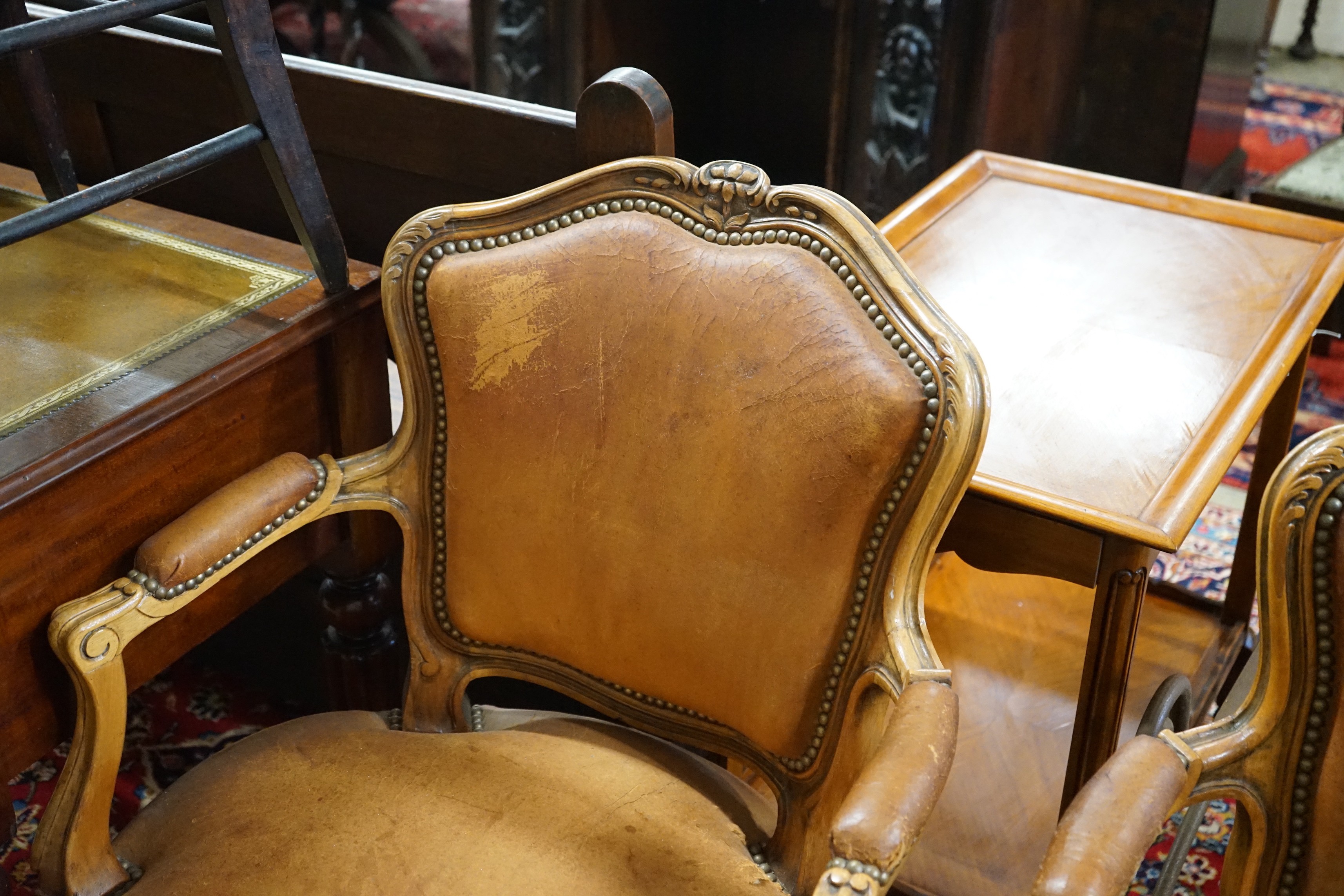 A pair of Louis XVI style carved walnut and tan leather fauteuils, width 62cm, depth 55cm, height 88cm